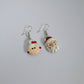 Pair of earrings with Santa Claus design on a light gray background with yellow flowers.